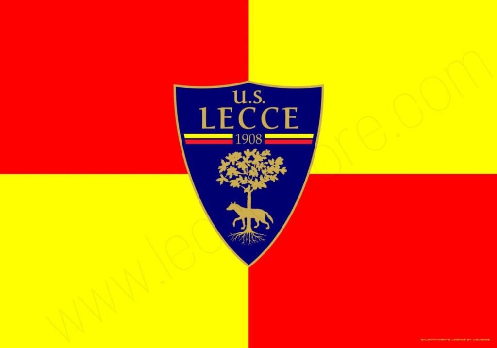 Logo del Lecce: scudo blu con un leone rampante al centro e scritta 'US Lecce' nella parte superiore. Sfondo rosso e giallo.
