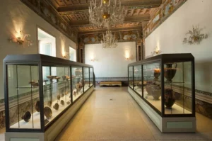 Spazio esposizione del Museo Claudio Faina, con espositori in una stanza con soffitto marrone, un lampadario e luci calde alle pareti.