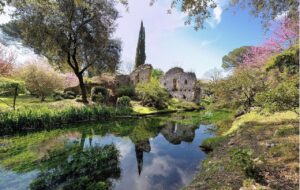 Veduta del Giardino di Ninfa con vegetazione rigogliosa, corsi d’acqua e rovine medievali immerse nel verde.