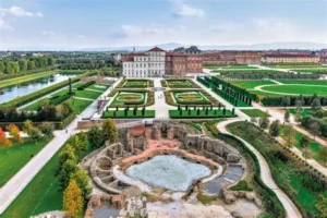 Facciata principale della Reggia di Venaria Reale con giardini curati in primo piano, fotografata in una giornata soleggiata