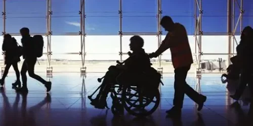 Immagine con un assistente aeroportuale che spinge una persona in sedia a rotelle all'interno dell'aeroporto.